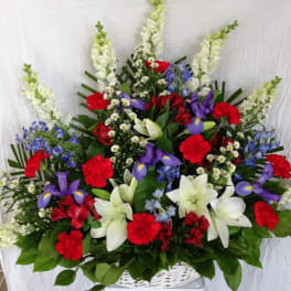 Large mixed flower arrangement in a white basket with red, white, and purple blooms