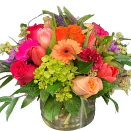 Bright mixed arrangement of roses, tulips, gerbera daisy and hydrangea in a clear glass vase