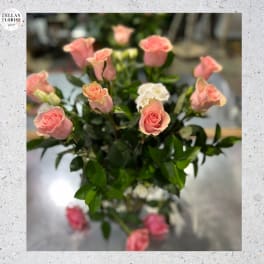 Tall arrangement of pink roses with a few white blooms in a clear glass vase.