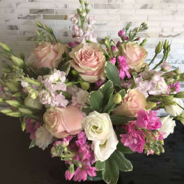 Rounded arrangement of blush roses, white blooms, and pink flowers in a glass vase