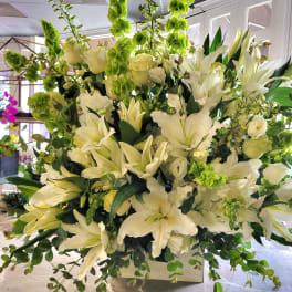 Large white floral arrangement with lilies and green accents in a white container