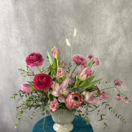 Pink and magenta flowers arranged in a white pedestal vase