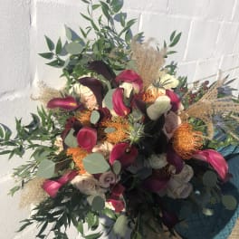 Large bouquet of burgundy calla lilies, cream roses, and orange protea with cascading greenery