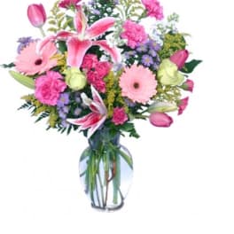 Mixed bouquet of pink lilies, tulips, carnations, and daisies in a clear glass vase