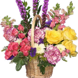 Wicker basket of yellow roses, pink spray roses, purple spikes, and mixed blooms in bright colors