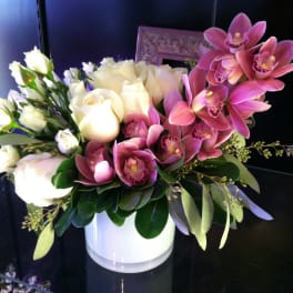 Low arrangement of white roses and pink orchids in a white cylinder vase