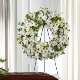 White floral wreath on a black stand with green accents