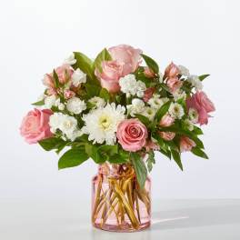 Pink roses and white daisies arranged in a pink glass vase