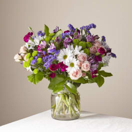 Mixed bouquet of daisies, roses, and purple filler flowers in a glass vase