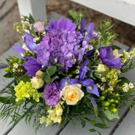 Low arrangement of purple hydrangea, irises, and cream roses with mixed accent blooms