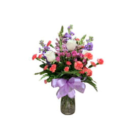 Bouquet of white roses, pink carnations, and purple flowers in a glass vase