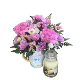 Pink mixed bouquet in a floral mug with a candle beside it