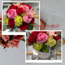 Compact arrangement of red roses, pink blooms, and green hydrangeas in a white vase