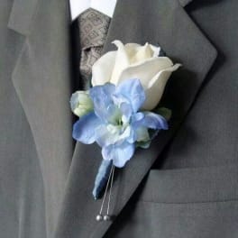 White rose and light blue flower boutonniere pinned to a gray suit lapel