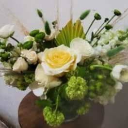 White and green floral arrangement with a yellow-centered rose in a vase
