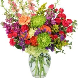 Tall mixed bouquet of bright roses, carnations, mums, and snapdragons in a clear glass vase