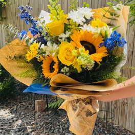 Bouquet of sunflowers, yellow roses, and blue flowers wrapped in paper