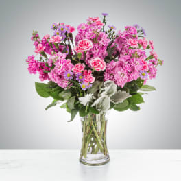 Tall glass vase of pink carnations and stock with small purple asters.