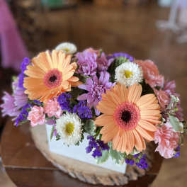 Bouquet of peach gerbera daisies, pink carnations, and purple flowers in a white box