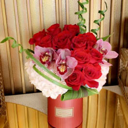 Red roses and pink orchids arranged in a striped hatbox