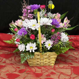 Basket arrangement of white daisies, pink and purple flowers, and a bee pick