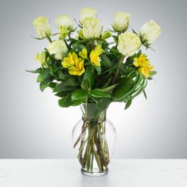 Clear glass vase with white roses and yellow alstroemeria arranged upright.