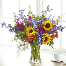 Bouquet of sunflowers, blue irises, and orange roses in a clear glass vase