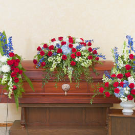Casket spray with red, white, and blue flowers on a wooden casket
