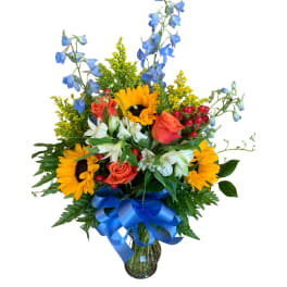 Bouquet of sunflowers, roses, and blue flowers in a glass vase with a blue ribbon