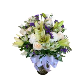 Bouquet of white lilies, roses, and purple filler flowers in a glass vase