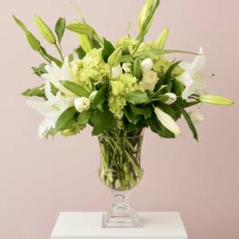 White lilies and green hydrangeas arranged in a clear pedestal vase