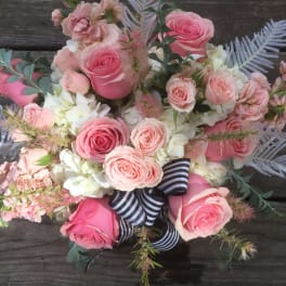 Pink roses and pale blooms arranged with a striped ribbon on wood