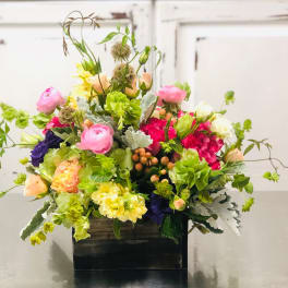 Mixed bouquet in a dark rectangular container with pink, yellow, white, and purple blooms