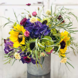 Mixed bouquet with sunflowers, purple hydrangea, and pink blooms in a gray vase