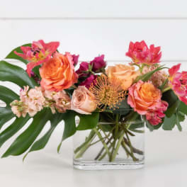 Mixed bouquet of pink and orange flowers in a clear glass vase