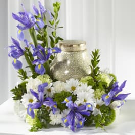 Purple irises and white daisies arranged around a gold urn candle.
