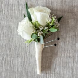 White rose boutonniere with small white filler flowers wrapped in ivory ribbon.
