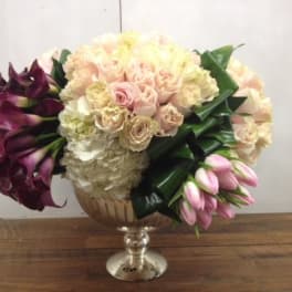 Bouquet of pale roses, hydrangeas, calla lilies, and pink tulips in a glass vase