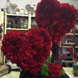 Two large heart-shaped red rose arrangements on a black base
