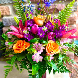 Colorful bouquet of orange roses, pink lilies, and purple flowers in a vase