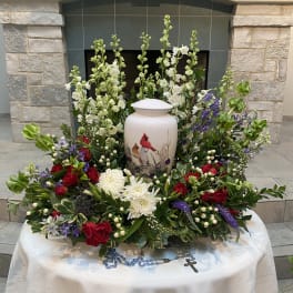 Floral funeral arrangement around a white urn with red, white, and purple flowers