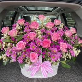 Pink roses and purple daisies arranged in a white basket with a pink ribbon