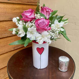 Pink roses and white flowers in a white vase with a heart design
