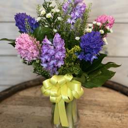 Mixed purple and pink bouquet in a glass vase with a yellow ribbon