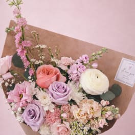 Handheld bouquet of pink, lavender, and white flowers wrapped in brown paper