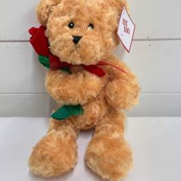 Tan teddy bear holding a red fabric rose with a tag on its ear
