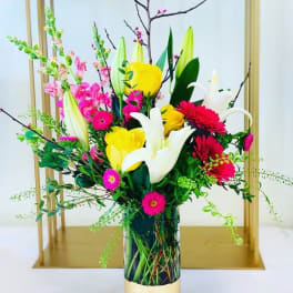Tall bouquet of yellow roses, white lilies, and pink flowers in a glass vase