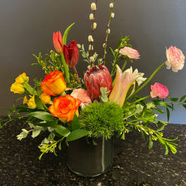 Mixed bouquet with roses, tulips, and a protea in a glass vase