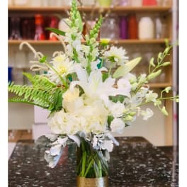 White floral arrangement in a gold vase with tall stems and fern accents