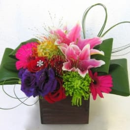 Colorful bouquet with lilies, roses, and gerbera daisies in a square vase